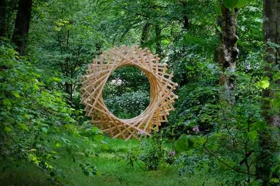 Image of a forest with a circular complex piece of land-art floating in the space between the trees
